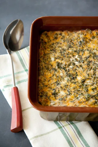 Paula Deen crustless spinach quiche baked golden with cheddar in a brown square baking dish beside a serving spoon