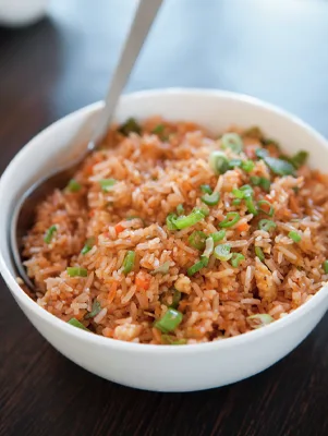 Paula Deen Cuts the Fat Dirty Rice with sliced scallions in a white bowl with a spoon