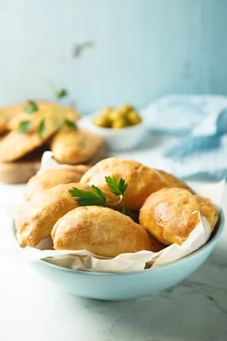 Golden Paula Deen deep-fried savory chicken pie half-moon pastries in a pale blue bowl with fresh parsley