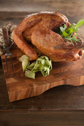 Paula Deen deep-fried turkey with golden brown skin on a wooden cutting board with fresh herbs and a carving fork