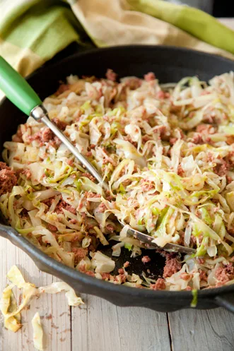 Paula Deen easy corned beef and cabbage cooking in a cast iron skillet with bacon and corned beef chunks