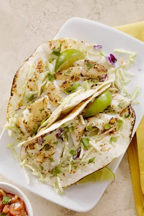 Paula Deen easy fish tacos with flaked grilled tilapia, shredded cabbage and lime wedges on corn tortillas on a white plate