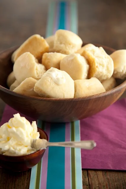 Paula Deen easy yeast rolls piled in a wooden bowl with a dish of whipped butter beside it