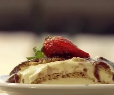 Slice of Paula Deen eclair cake with graham cracker layers, vanilla pudding and chocolate frosting topped with a fresh strawberry