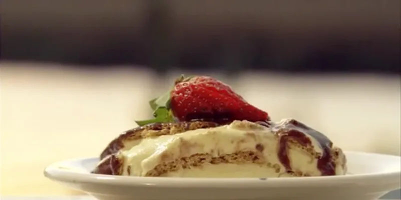 Slice of Paula Deen eclair cake with graham cracker layers, vanilla pudding and chocolate frosting topped with a fresh strawberry