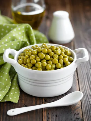 Paula Deen English Peas in a white ceramic dish with handles beside a white spoon on a rustic wooden table