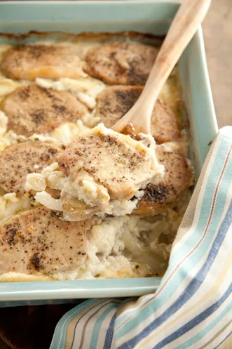 Paula Deen farmer's pork chops casserole with browned pork chops over creamy sliced potatoes in a blue baking dish