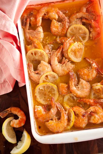 Paula Deen fiery Cajun shrimp baked in a white dish with lemon slices in a spicy butter sauce