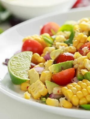 Paula Deen fire roasted corn salsa with charred corn kernels, diced tomato, avocado, red onion and a lime wedge on a white plate
