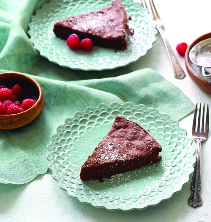 Paula Deen flourless chocolate fudge cake slices dusted with powdered sugar on mint green plates with fresh raspberries