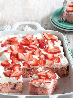 Paula Deen fresh strawberry sheet cake in a white baking dish topped with cream cheese frosting and sliced fresh strawberries