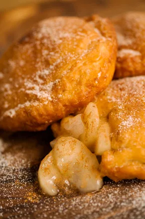 Paula Deen fried apple pies dusted with powdered sugar, one broken open to show the cinnamon apple filling