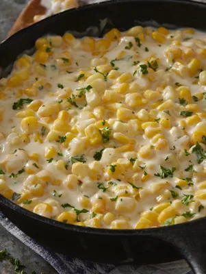 Paula Deen fried creamed corn in a black cast iron skillet topped with fresh chopped herbs