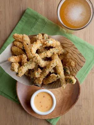 Paula Deen fried green bean bundles golden and crispy in a paper-lined basket with a dipping sauce and a glass of beer