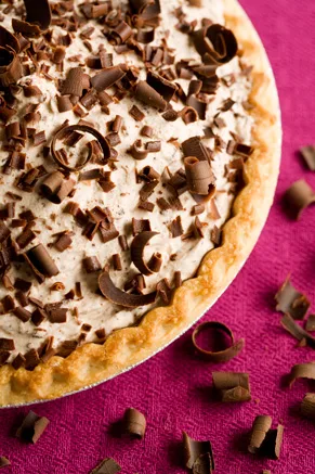 Paula Deen frozen chocolate mousse pie in a golden crust topped with chocolate curls and shavings on a pink background