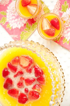 Paula Deen fruit punch in a glass punch bowl with fresh strawberries floating on top and two small glasses of punch garnished with strawberries