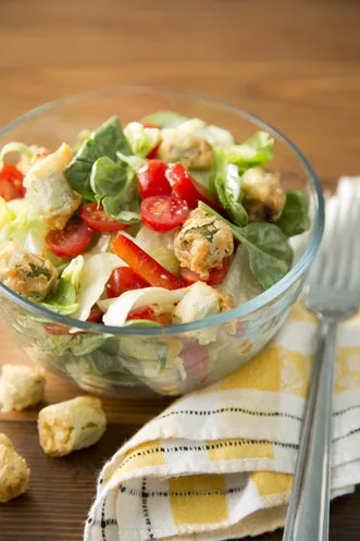 Paula Deen garden salad with fried okra croutons, spinach, cherry tomatoes and red pepper in a glass bowl