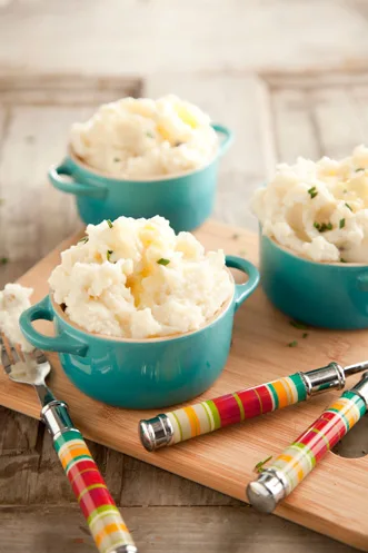 Paula Deen garlic mashed potatoes served in small teal ramekins topped with butter and chives on a wooden board