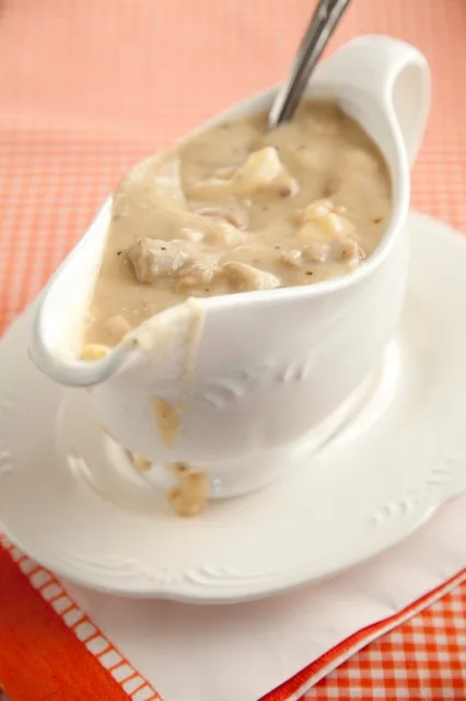 Paula Deen giblet gravy with chopped giblets and sliced egg in a white gravy boat with a spoon