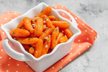 Paula Deen glazed baby carrots in a white serving dish with a glossy brown sugar glaze and herbs on an orange napkin