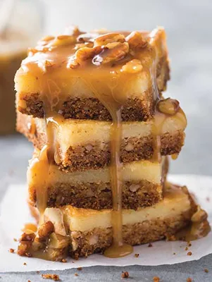 Stack of Paula Deen gooey butter pecan cake squares with a pecan crust, soft filling and caramel pecan sauce dripping down the sides