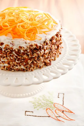 Paula Deen Grandma Hiers' Southern carrot cake on a white pedestal stand with chopped pecans on the sides and shredded carrot curls on top