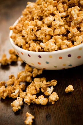 Paula Deen Grandma Paul's caramel corn piled in a polka dot bowl with loose pieces on a wooden table