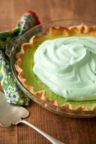 Paula Deen green grits pie with pale green whipped cream in a glass pie plate with a fluted crust