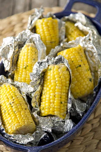 Paula Deen grilled corn on the cob halves wrapped in foil with cilantro butter in a blue baking dish