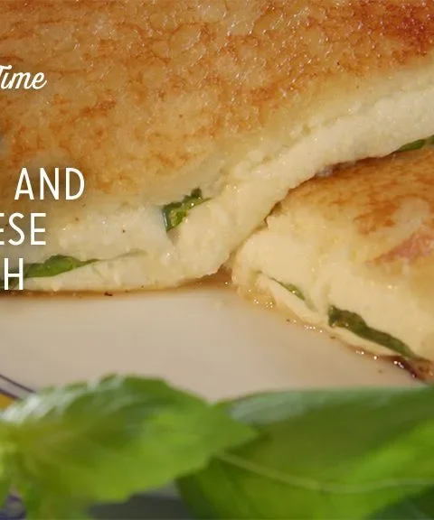 Paula Deen grilled mozzarella and goat cheese sandwich cut in half with melted cheese and fresh basil on a plate