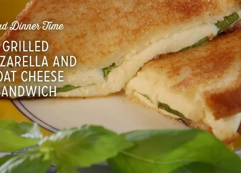 Paula Deen grilled mozzarella and goat cheese sandwich cut in half with melted cheese and fresh basil on a plate