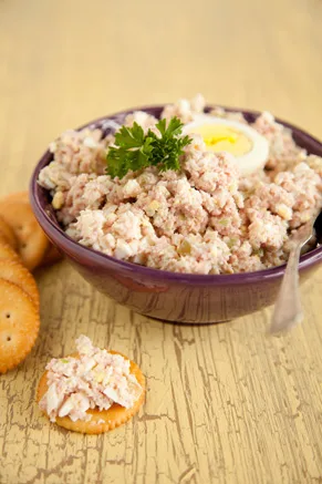 Paula Deen ham salad in a purple bowl topped with parsley and a halved hard-boiled egg, with a ham salad cracker beside it