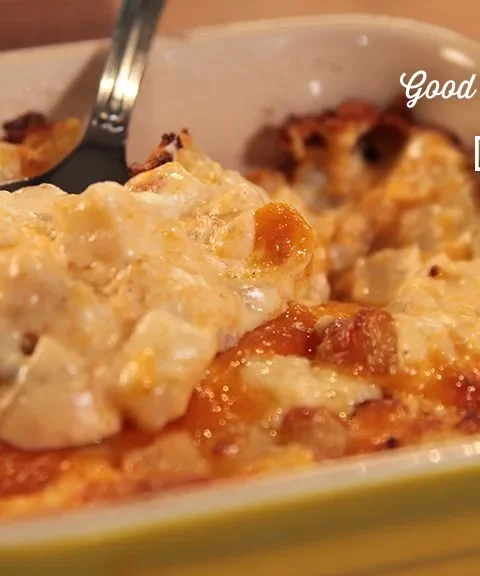 Paula Deen hash brown potato casserole with a golden browned cheddar top in a yellow baking dish with a spoon