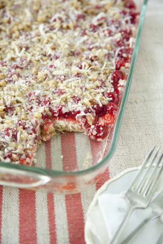 Paula Deen holiday cherry cheesecake in a glass baking dish with cherry topping and walnut coconut crumbs, one square cut out