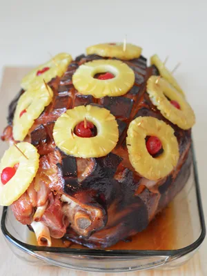 Paula Deen holiday glazed ham topped with pineapple rings, maraschino cherries and toothpicks in a glass baking dish