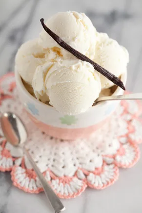 Paula Deen homemade vanilla ice cream scooped into a bowl and topped with a vanilla bean on a crocheted doily