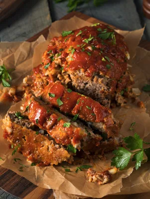 Sliced Paula Deen homestyle meatloaf with a glossy tomato glaze and fresh parsley on parchment paper