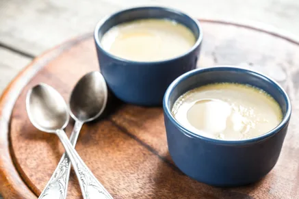 Two navy blue ramekins of Paula Deen honey lemon pots de creme on a wooden board with two vintage spoons