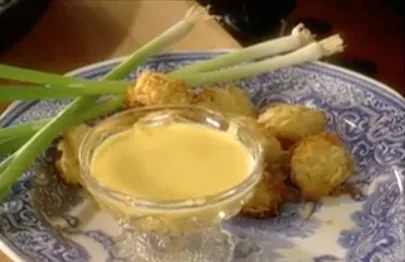Paula Deen honey mustard dipping sauce in a glass bowl beside crispy potato bites and green onions on a blue and white plate