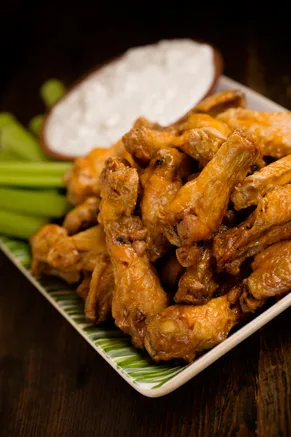 Paula Deen hot buffalo wings piled on a square plate with celery sticks and a bowl of creamy Roquefort dip