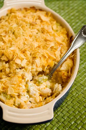Paula Deen hot chicken salad baked in an oval dish with a golden crushed potato chip and cheddar topping and a serving spoon