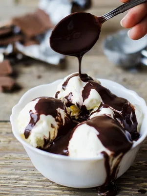 Paula Deen hot fudge chocolate sauce being spooned over scoops of vanilla ice cream in a white bowl