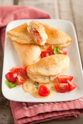Paula Deen hot tomato tart appetizers, golden folded biscuit turnovers on a white platter with diced fresh tomato and basil, one cut open to show the filling
