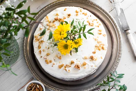 Paula Deen hummingbird cake with cream cheese frosting, chopped nuts and yellow flowers on a silver platter