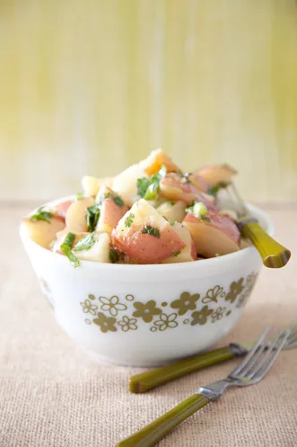 Paula Deen Italian potatoes, chunks of red potato with chopped parsley in a white bowl with a green floral pattern