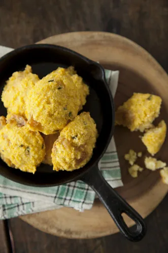 Paula Deen jalapeño cracklin' cornbread pones in a small cast iron skillet on a wooden board with a green checkered towel