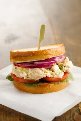 Paula Deen Jamie's chicken salad sandwich with red onion, tomato and spinach on toasted bread, held with a bamboo pick