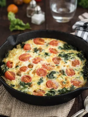 Paula Deen kale and bacon frittata in a cast iron skillet topped with chopped cherry tomatoes and melted cheese