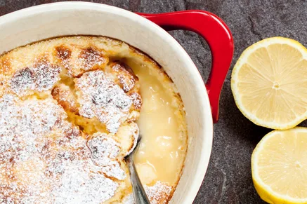 Paula Deen lemon curd pudding dusted with powdered sugar in a red baking dish next to halved lemons