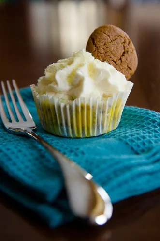 Paula Deen lemon poppyseed cheesecake cupcake topped with ginger whipped cream and a gingersnap cookie on a teal napkin